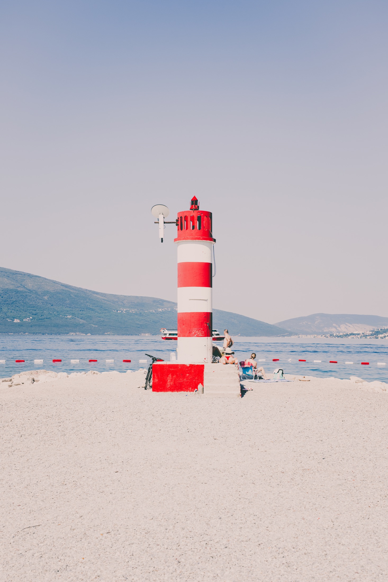 Small red and white lighthouse beside a calm beach