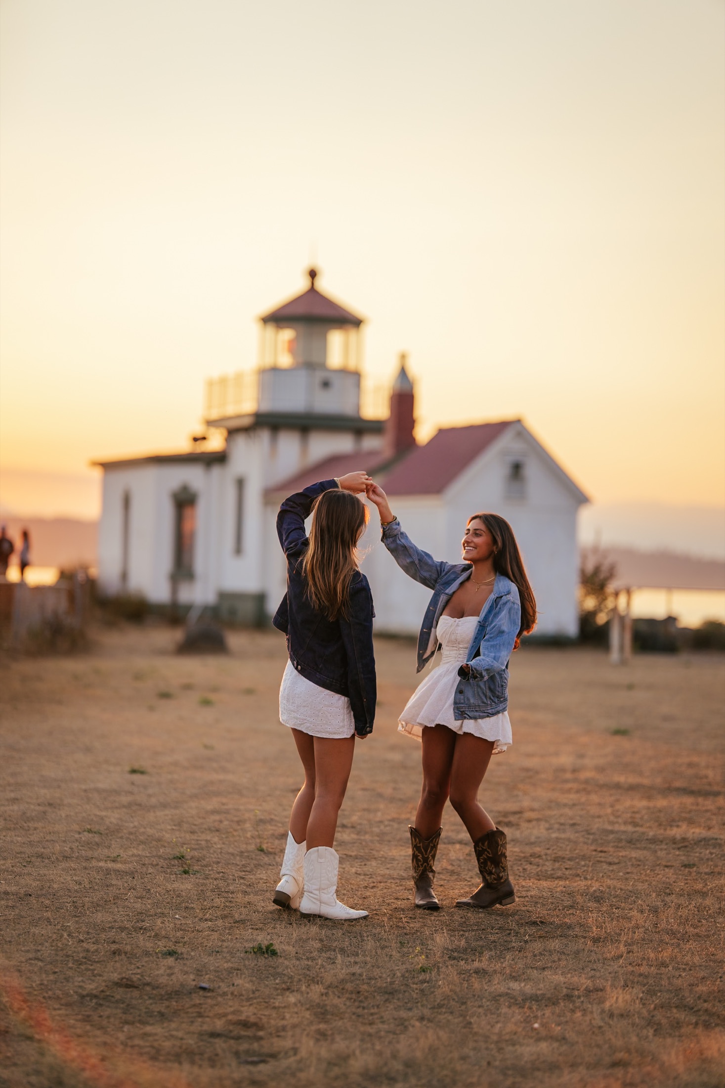 Two friends dancing in front of a lighthouse at sunset