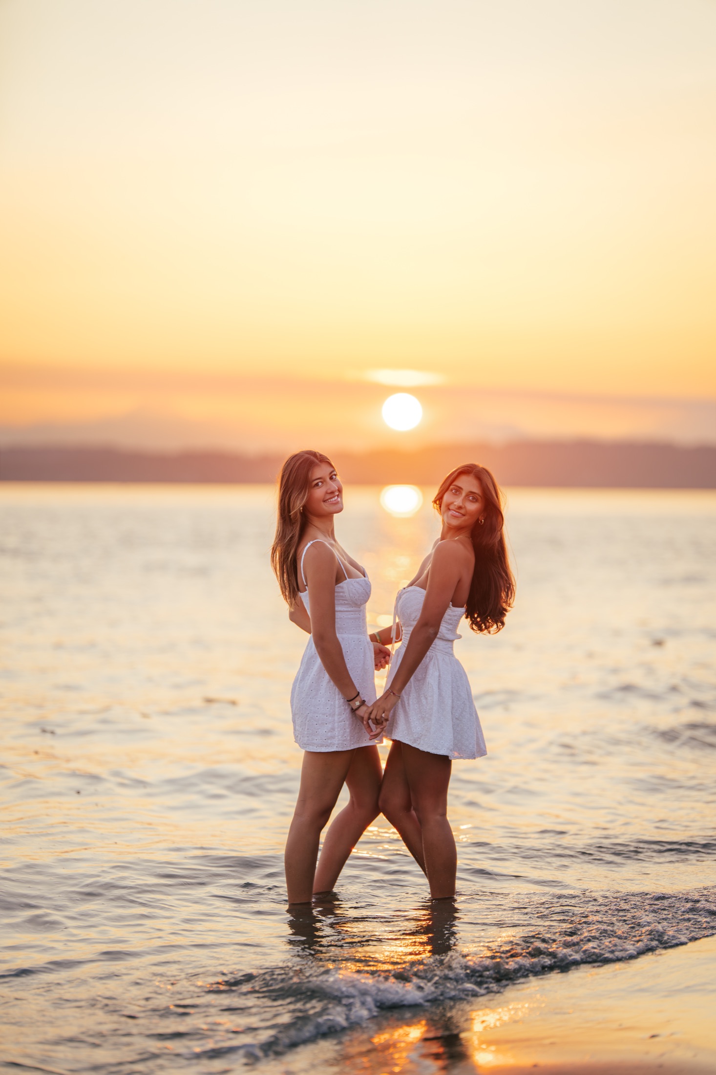 Two friends holding hands in the water beneath the setting sun