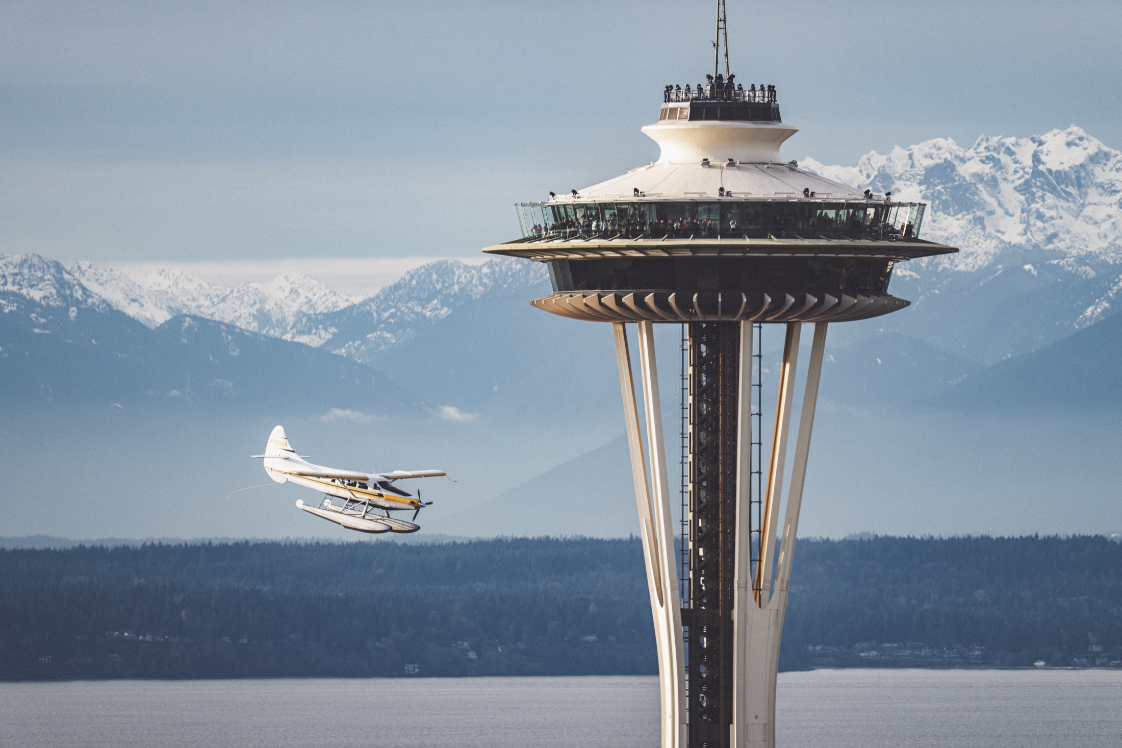 A seaplane passing the Space Needle with the Olympic Mountains behind