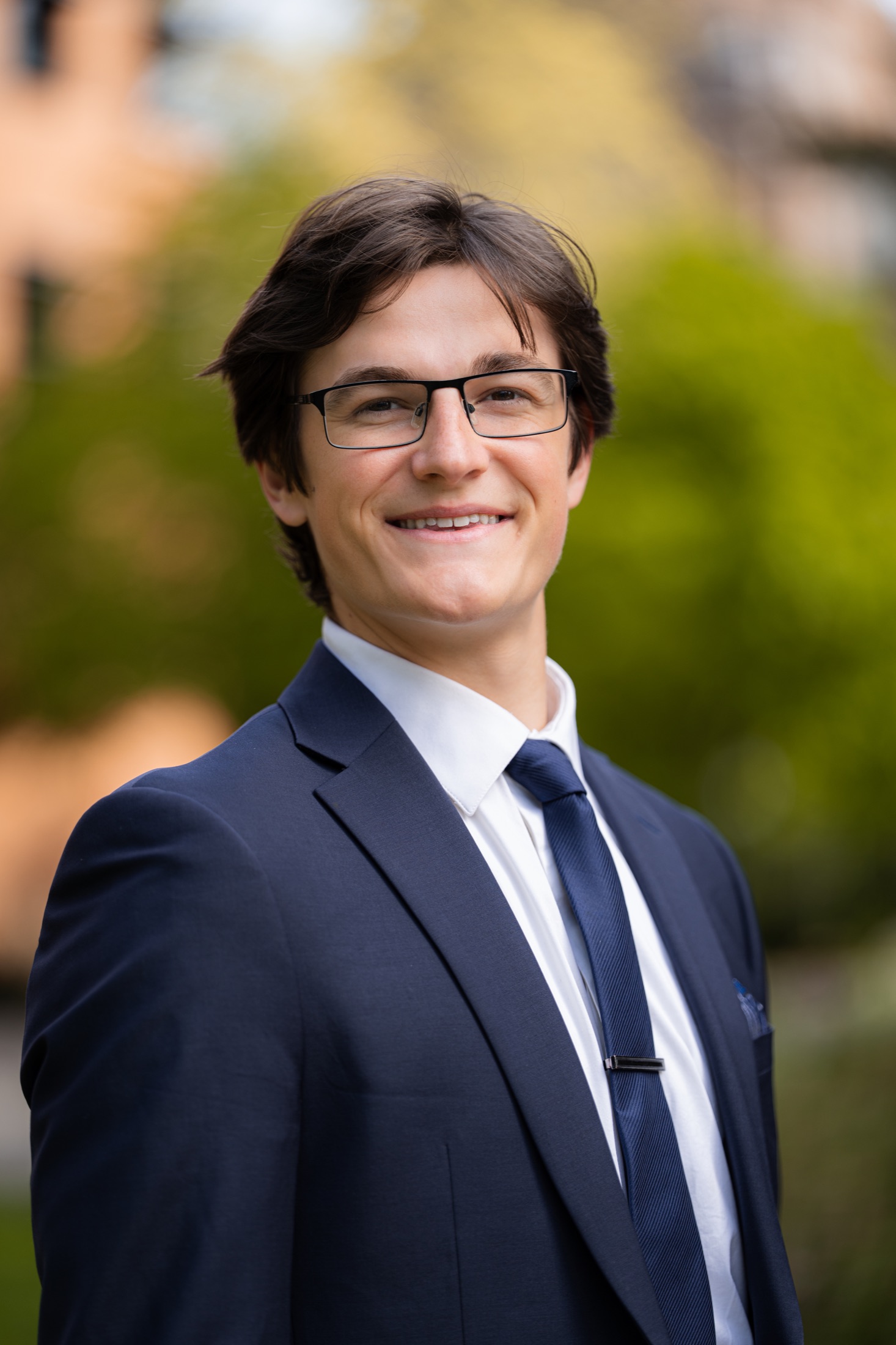 Man with glasses wearing a navy suit outdoors